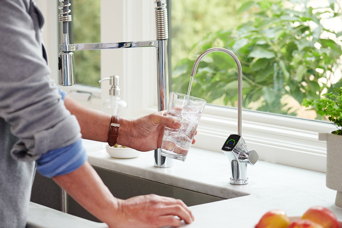Person filling glass at kitchen drinking water system